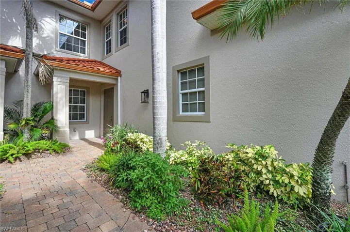 Stucco exterior with terracotta-style roof accents, multi-pane windows, and a paver stone walkway leading to the entryway