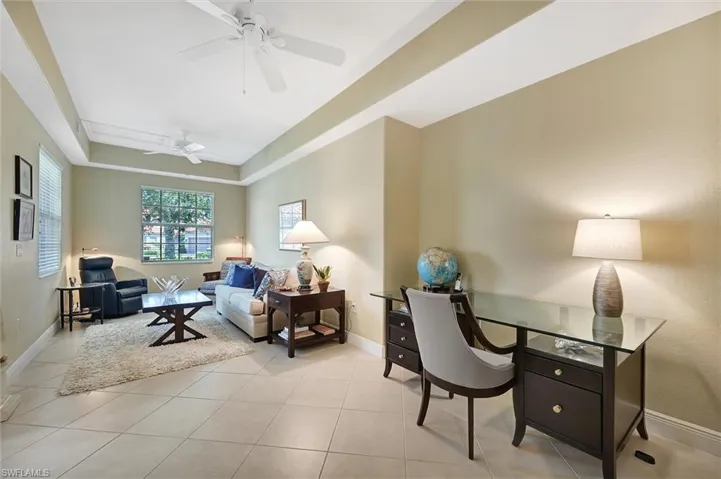 Tray ceiling with dual ceiling fans, tile flooring, and oversized window with horizontal blinds
