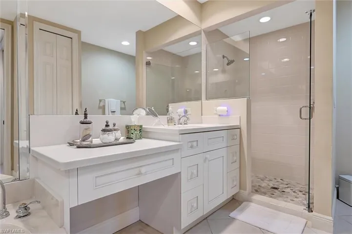 Bathroom featuring a white vanity with a countertop, recessed lighting, a large wall-mounted mirror, and a walk-in shower with a glass enclosure and pebble-style stone flooring