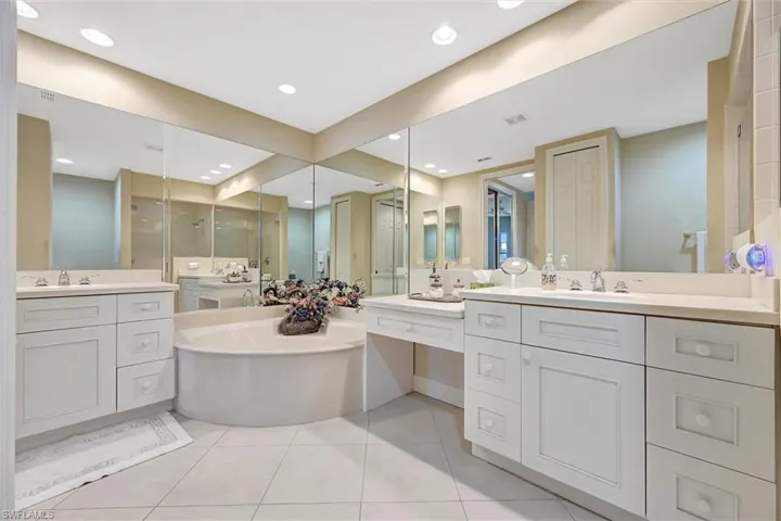 Bathroom featuring dual vanity cabinetry with light-colored countertops, large wall-to-wall mirrors, recessed lighting, and a built-in soaking tub
