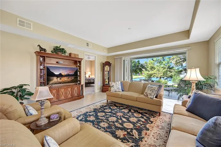 Living area featuring a tray ceiling, expansive multi-panel sliding glass doors, built-in wooden media cabinetry, and tile flooring