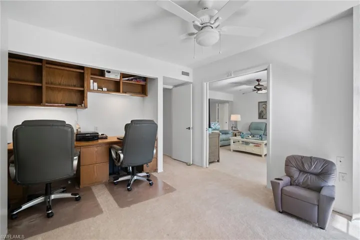 Carpeted office space with built in desk and ceiling fan