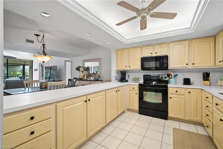 Kitchen with black appliances, light tile patterned flooring, a tray ceiling, and ceiling fan