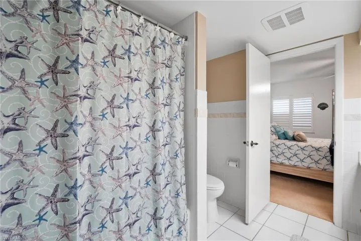 Bathroom with tile walls, tile patterned flooring, a shower with curtain, and toilet