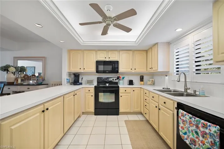 Kitchen with ceiling fan, a raised ceiling, sink, backsplash, and black appliances
