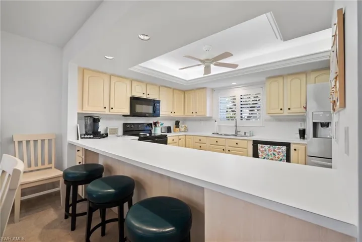 Kitchen featuring ceiling fan, sink, kitchen peninsula, black appliances, and a breakfast bar
