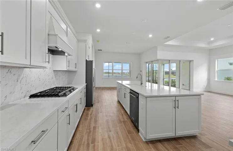 Kitchen with appliances with stainless steel finishes, white cabinetry, custom exhaust hood, a raised ceiling, and a center island with sink