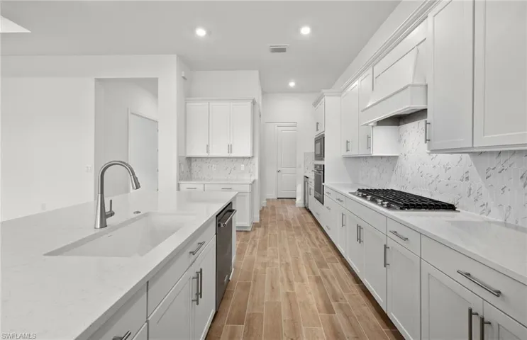 Kitchen featuring stainless steel appliances, sink, white cabinets, and custom range hood