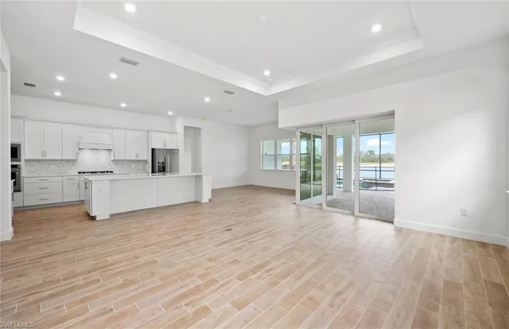 Unfurnished living room with ornamental molding, a raised ceiling, sink, and light wood-type flooring