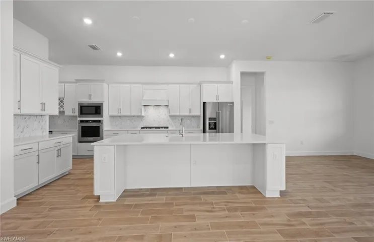 Kitchen with a center island with sink, custom exhaust hood, white cabinets, and appliances with stainless steel finishes