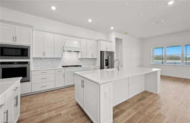 Kitchen with stainless steel appliances, an island with sink, custom range hood, and white cabinetry