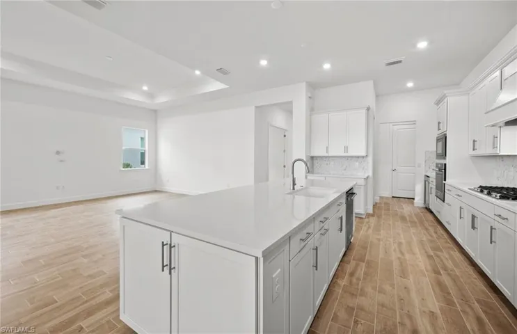 Kitchen featuring white cabinetry, stainless steel appliances, sink, and a center island with sink