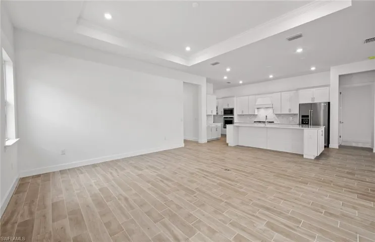 Unfurnished living room with a raised ceiling, crown molding, sink, and light hardwood / wood-style flooring