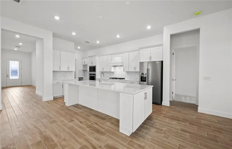 Kitchen featuring premium range hood, white cabinetry, appliances with stainless steel finishes, an island with sink, and light hardwood / wood-style floors