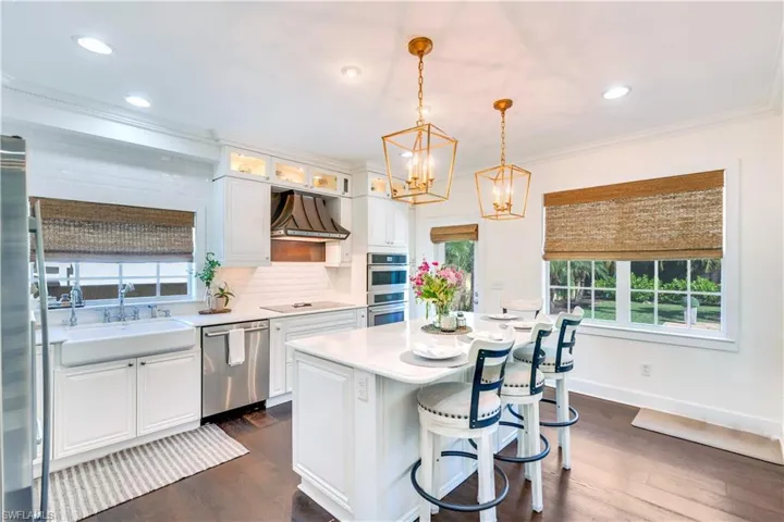 Kitchen featuring dark wood-type flooring, custom range hood, backsplash, white cabinetry, and appliances with stainless steel finishes