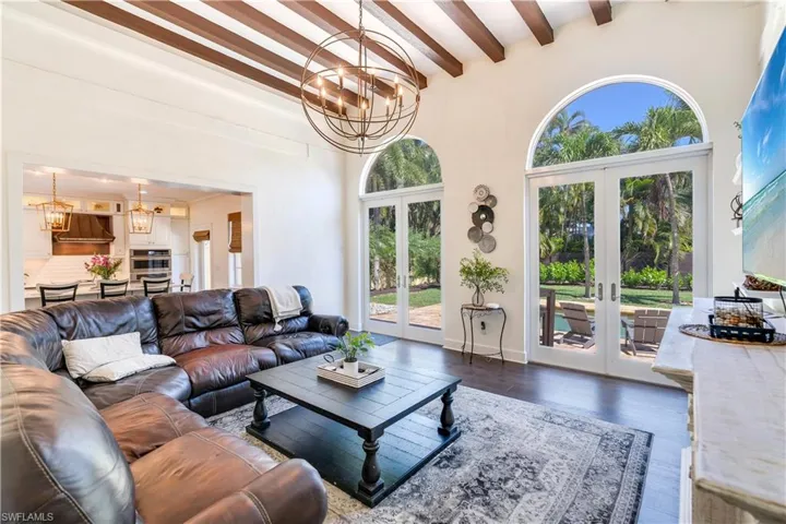 Living room with dark hardwood / wood-style floors, a notable chandelier, beam ceiling, and french doors