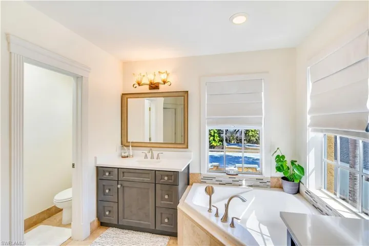 Bathroom with tile floors, a relaxing tiled bath, large vanity, and toilet