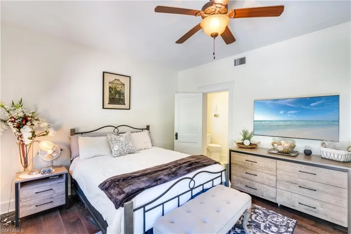 Bedroom featuring connected bathroom, dark wood-type flooring, ceiling fan, and a water view