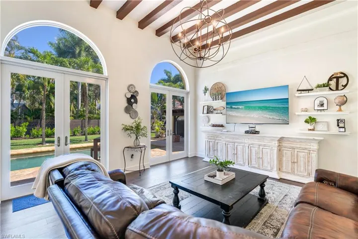 Living room with a notable chandelier, beam ceiling, french doors, and hardwood / wood-style flooring