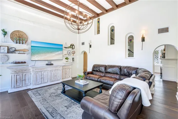 Living room with beamed ceiling, a towering ceiling, dark hardwood / wood-style flooring, and a chandelier