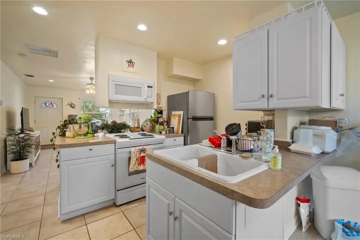 Kitchen featuring kitchen peninsula, white appliances, white cabinetry, and sink