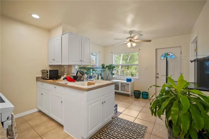 Kitchen with white cabinetry, sink, ceiling fan, and light tile patterned flooring