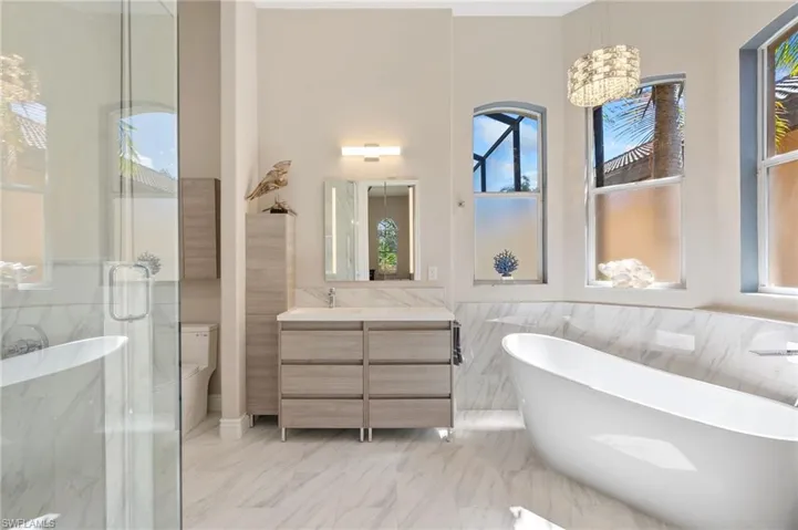Bathroom featuring a freestanding tub, toilet, vanity, marble finish floor, and a shower stall