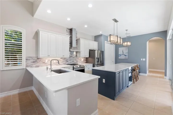 Kitchen featuring arched walkways, stainless steel appliances, a sink, a kitchen island, and wall chimney exhaust hood