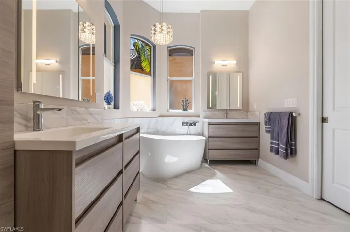 Full bath with a freestanding tub, a notable chandelier, two vanities, a sink, and marble finish floor