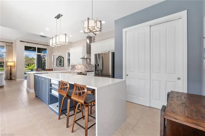 Kitchen featuring light tile patterned floors, stainless steel appliances, white cabinetry, wall chimney range hood, and tasteful backsplash