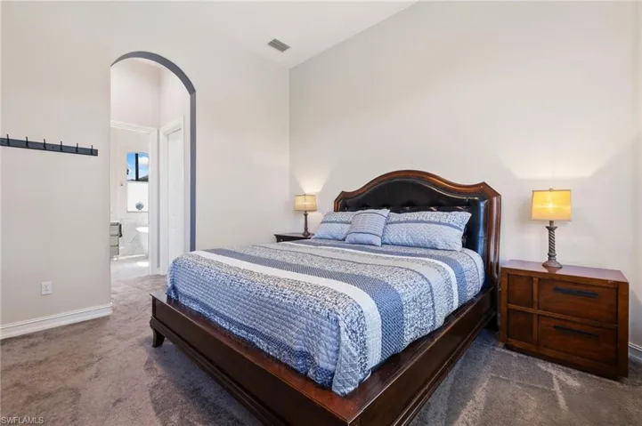 Carpeted bedroom featuring arched walkways, visible vents, baseboards, and ensuite bathroom