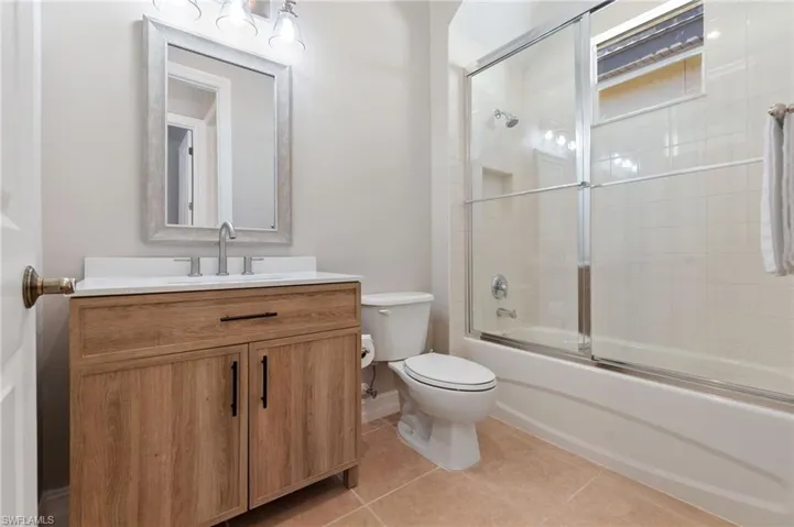 Bathroom featuring toilet, tile patterned flooring, combined bath / shower with glass door, and vanity