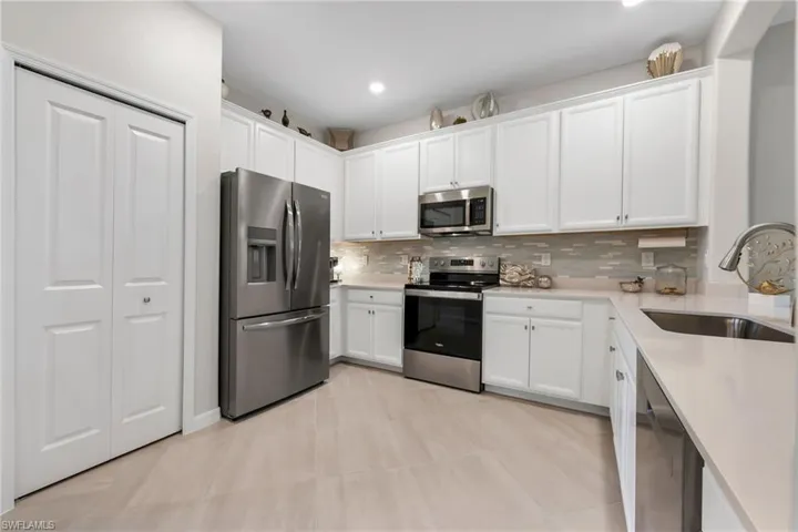 Kitchen featuring stainless steel appliances, white cabinetry, light quartz counters, and decorative backsplash