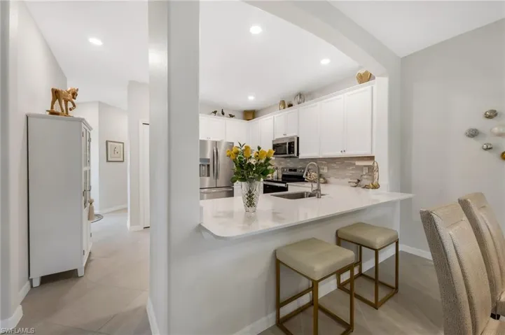 Kitchen with stainless steel appliances, decorative backsplash, a peninsula, white cabinets, and a breakfast bar area