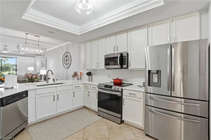 Kitchen with stainless steel appliances, a raised ceiling, crown molding, white cabinetry, and pendant lighting