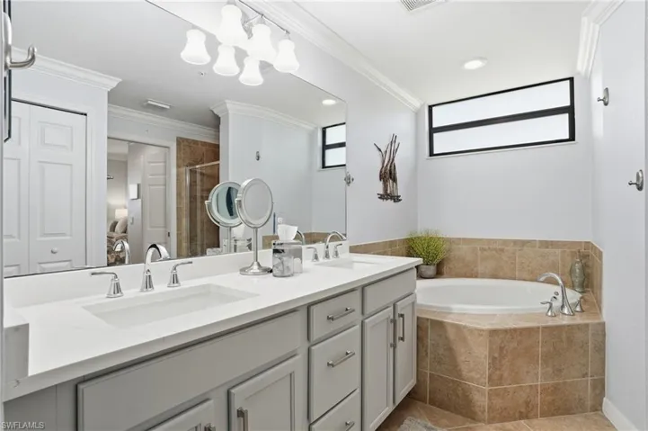 Ensuite bathroom featuring double vanity, crown molding, a bath, a shower stall, and light tile patterned flooring