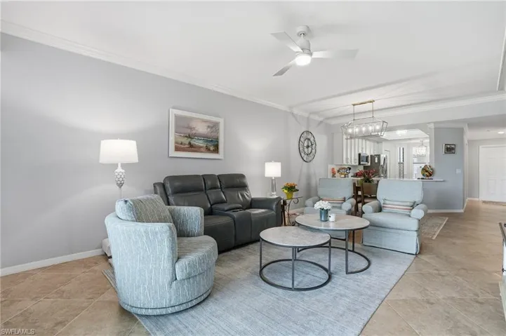 Living area with ornamental molding, a ceiling fan, light tile patterned floors, and a chandelier