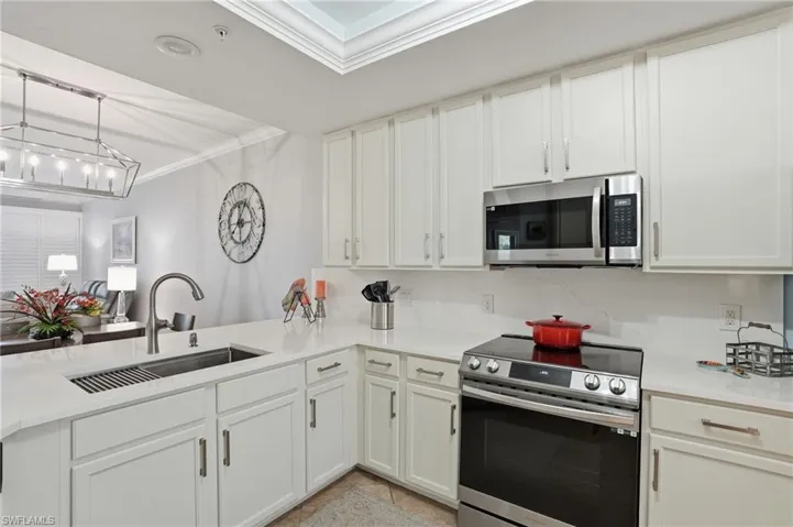 Kitchen featuring stainless steel appliances, white cabinets, crown molding, pendant lighting, and light stone countertops