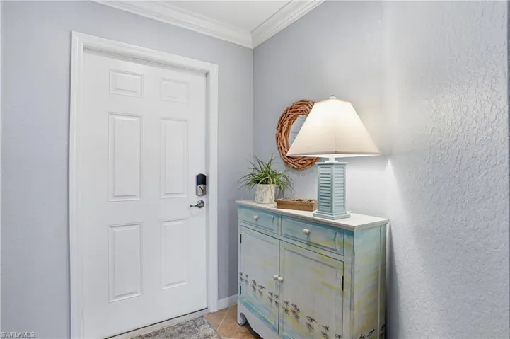 Foyer entrance with ornamental molding, a textured wall, and light tile patterned floors