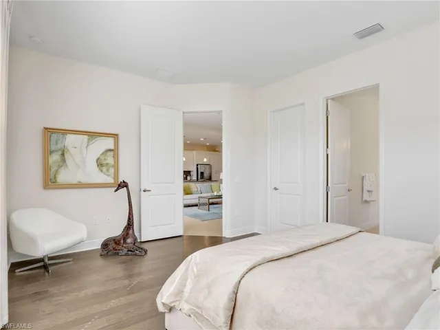 Bedroom with stainless steel fridge, baseboards, visible vents, ensuite bath, and wood finished floors