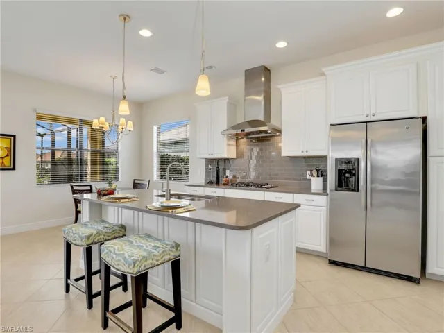 Kitchen featuring light tile patterned flooring, stainless steel appliances, a sink, wall chimney range hood, and backsplash