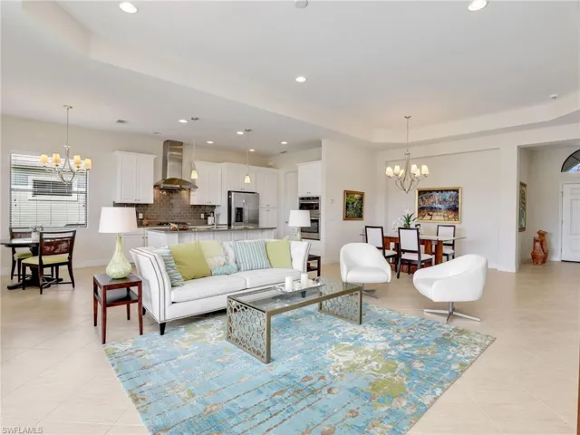 Living area with a tray ceiling, light tile patterned floors, a notable chandelier, and recessed lighting