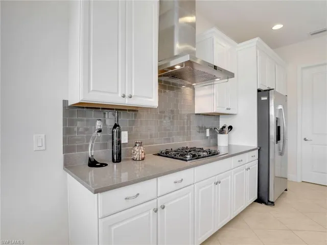 Kitchen with gas stovetop, visible vents, white cabinetry, ventilation hood, and stainless steel refrigerator with ice dispenser