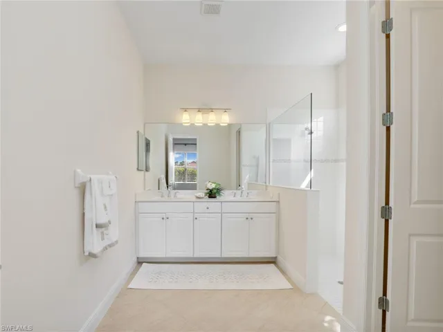Bathroom with double vanity, visible vents, a sink, baseboards, and walk in shower
