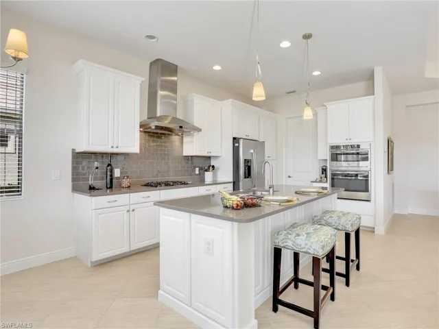 Kitchen with wall chimney exhaust hood, appliances with stainless steel finishes, white cabinets, and tasteful backsplash