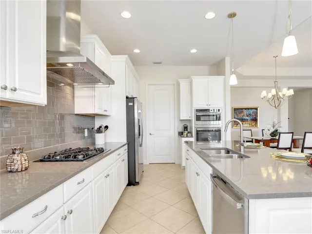 Kitchen with stainless steel appliances, a sink, white cabinets, wall chimney range hood, and tasteful backsplash