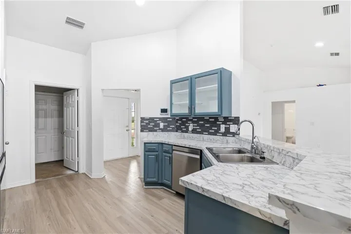 Kitchen with blue cabinetry, a peninsula, glass insert cabinets, lofted ceiling, and light wood finished floors