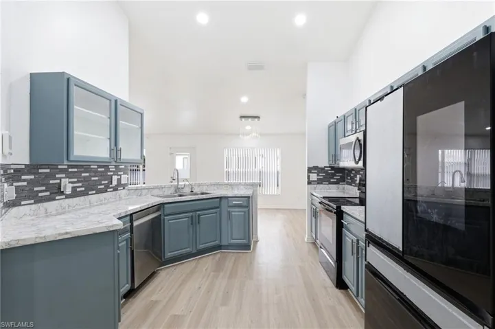 Kitchen with stainless steel appliances, a peninsula, blue cabinets, glass fronted cabinets, and light wood finished floors