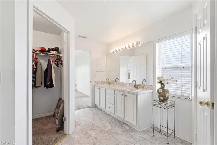 Bathroom with double vanity, light marble finish flooring, and a spacious closet
