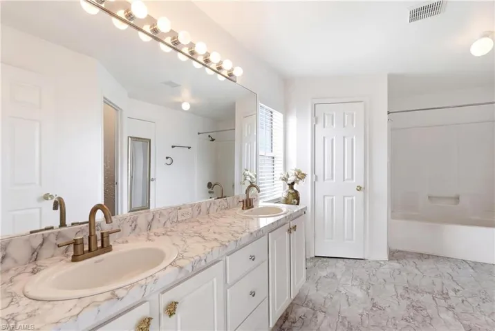 Bathroom with double vanity, light marble finish flooring, and shower / washtub combination